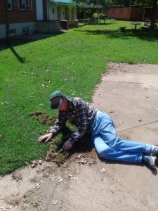 Nigel lies on the ground to trim edges of lawn around the Tim Hickman Memorial Hall at Pevensey Place. 